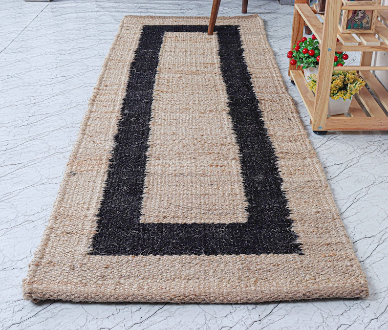 Op de afbeelding: Een vloerkleed van natuurlijke vezels met een zwarte rand. Het vloerkleed is gemaakt van jute en heeft een rechthoekige vorm.