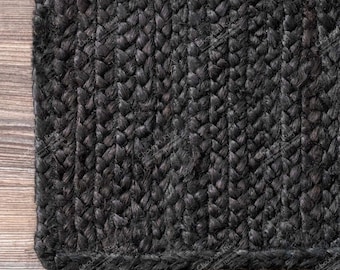 May include: Close-up of a black braided rug with a textured surface. The rug is made of natural fibres and has a simple, modern design.
