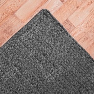 Puede incluir: Una alfombra tejida de color gris oscuro con una superficie texturizada. La alfombra está colocada sobre un suelo de madera clara.