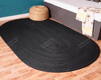 May include: An oval-shaped area rug featuring a solid black color and a braided texture. The rug is constructed from woven fibers arranged in concentric oval patterns, creating a uniform and dense surface across the entire floor covering.