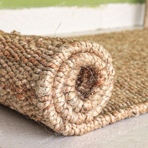 May include: Close-up of a rolled up natural fiber rug. The rug is made of tightly woven, light brown fibers. The rug is rolled up tightly, showing the texture of the fibers.