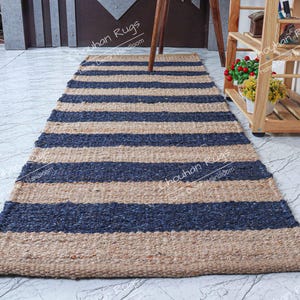 May include: A rectangular rug with alternating horizontal stripes of navy blue and tan. The rug is made of a woven material and is placed on a light-colored tiled floor. The rug is a home decor item.