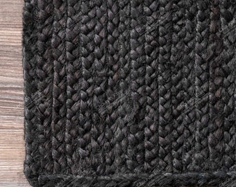 May include: A rectangular area rug featuring a solid black colour and a thick, braided texture. The rug is constructed from tightly woven, interlaced strands that create a uniform, repeating pattern across the entire surface of the floor covering.