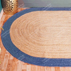 K&ouml;nnte beinhalten: Ein ovaler Teppich aus Naturfasern mit einem blauen Rand. Der Teppich ist aus Jute und hat eine gewebte Struktur.