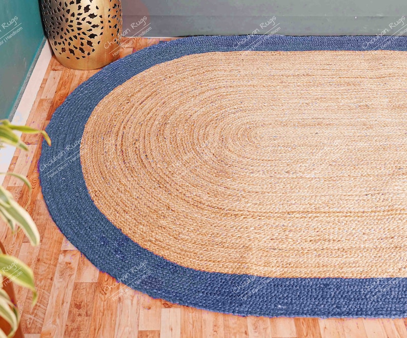 K&ouml;nnte beinhalten: Ein ovaler Teppich aus Naturfasern mit einem blauen Rand. Der Teppich ist aus Jute und hat eine gewebte Struktur.
