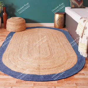 K&ouml;nnte beinhalten: Ein ovaler Teppich aus Naturfasern mit einem blauen Rand. Der Teppich ist aus Jute und hat eine nat&uuml;rliche, erdige Optik. Er ist perfekt, um jedem Raum einen Hauch von W&auml;rme und Textur zu verleihen.