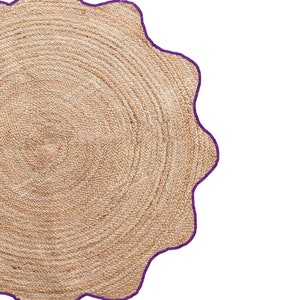 May include: A round, woven jute rug with a scalloped edge. The rug is a natural tan color with a dark purple border. The rug's design features concentric circles, creating a textured surface.