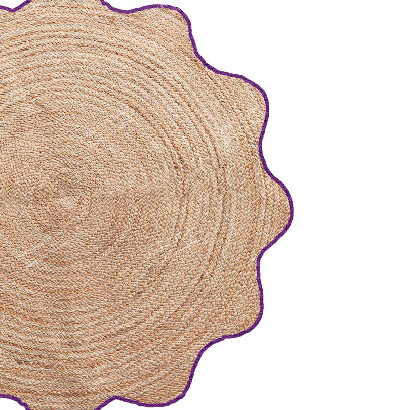 May include: A round, woven jute rug with a scalloped edge. The rug is a natural tan color with a dark purple border. The rug's design features concentric circles, creating a textured surface.