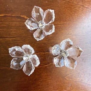 May include: Three clear glass flower-shaped embellishments with a crystal centre. Each flower has five petals.