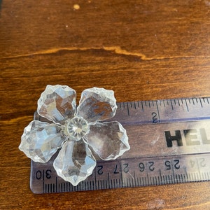 May include: A clear crystal flower with five petals and a small crystal centre. The flower is approximately 5 cm wide and is resting on a ruler.