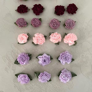 May include: Assortment of small fabric flowers in various colors, including red, pink, purple, and lavender. The flowers are all made of satin ribbon and have a simple, elegant design.