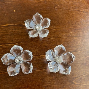 May include: Three clear crystal flower-shaped embellishments with a small rhinestone in the centre of each flower.