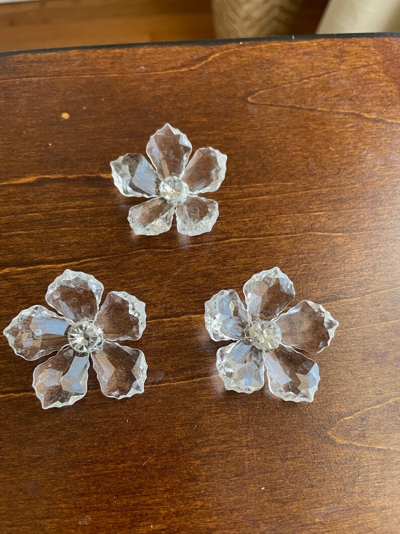 May include: Three clear crystal flower-shaped embellishments with a small rhinestone in the centre of each flower.