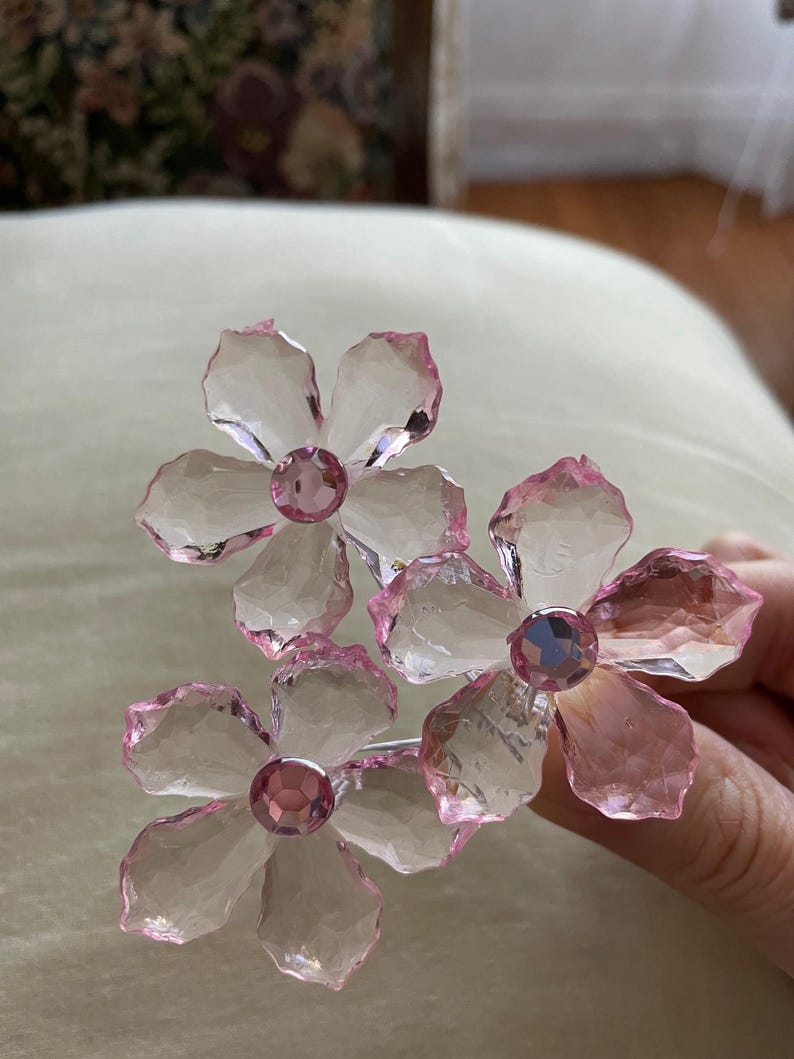 May include: Three pink crystal flower hair clips with clear centres and pink rhinestones in the centre of each flower.