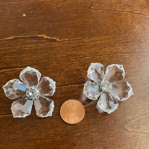May include: Two clear crystal flower-shaped embellishments with a faceted design. The embellishments are approximately the size of a UK penny.