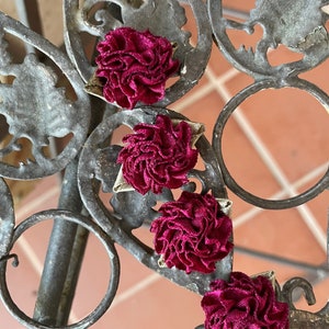 May include: Four burgundy fabric flowers with a ruffled texture, arranged in a row on a metal surface.