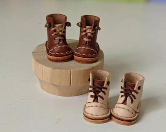 Könnte beinhalten: Vier Paar Miniatur-Lederstiefel in Braun und Creme. Die Stiefel haben Schnürsenkel und stehen auf einer Holzplattform.