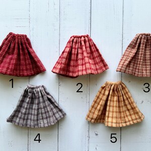 Pu&ograve; includere: Cinque gonne a quadri per bambole in diversi colori e motivi. Le gonne sono numerate da 1 a 5.