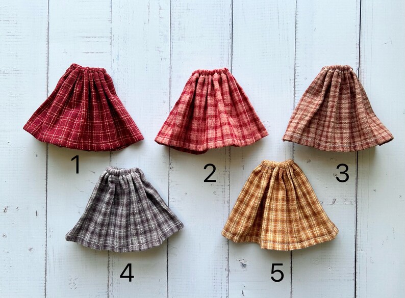 Pu&ograve; includere: Cinque gonne a quadri per bambole in diversi colori e motivi. Le gonne sono numerate da 1 a 5.