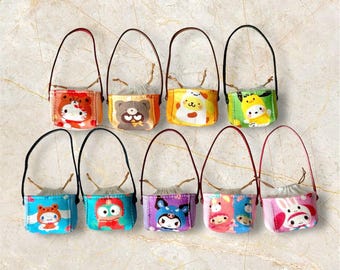 May include: A collection of ten small, colorful tote bags with black or red handles. Each bag features a different cartoon character design, including bears, cats, and other cute creatures. The bags have a drawstring closure and are set against a light-colored background.