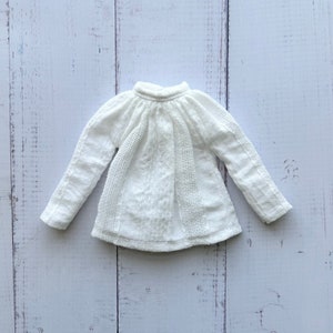 Può includere: Camicia bianca a maniche lunghe con scollo arricciato e tessuto strutturato.