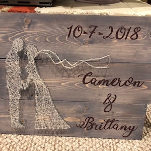 Puede incluir: Un letrero de madera con un diseño de arte de hilo de un par, la fecha 10-7-2018 y los nombres Cameron & Brittany.