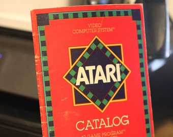 May include: A red Atari Video Computer System catalog with a blue and green diamond logo and the text "CATALOG 49 GAME PROGRAM CARTRIDGES".