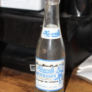 May include: A clear glass bottle with a blue and white label that reads "Howels Beverages with that good old fashioned flavour" and "Contents 7 fl. oz."
