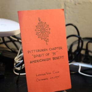 Puede incluir: Un folleto naranja con texto negro y un emblema de las Hijas de la Revolución Americana. El texto dice "Pittsburgh Chapter Spirit of '75 Americanism Benefit" y "Longue Vue Club October 24, 1975."