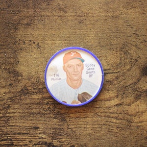 May include: A vintage baseball card featuring Bobby Gene Smith, a Philadelphia Phillies player. The card is blue and white with a picture of Smith in his uniform. The text on the card reads "176 Phillies" and "Bobby Gene Smith OF".