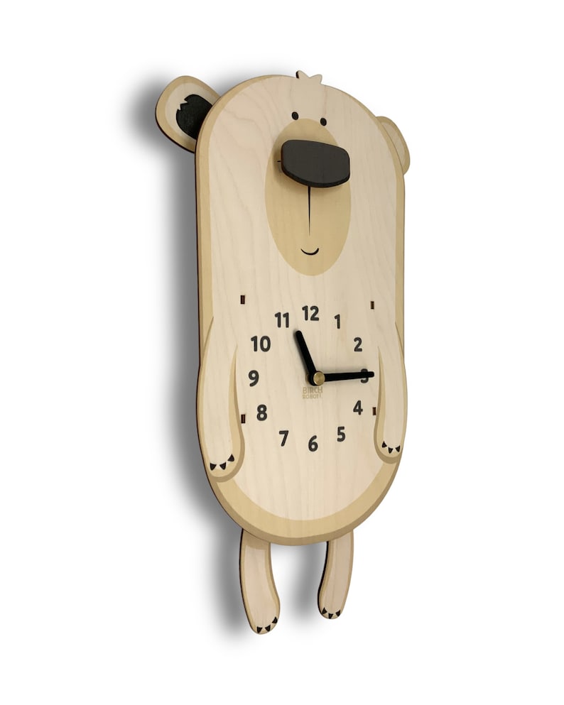 K&ouml;nnte beinhalten: Eine h&ouml;lzerne Wanduhr in Form eines B&auml;ren mit einer schwarzen Nase und schwarzen Zeigern. Das Zifferblatt der Uhr hat schwarze Zahlen und einen schwarzen Rahmen.