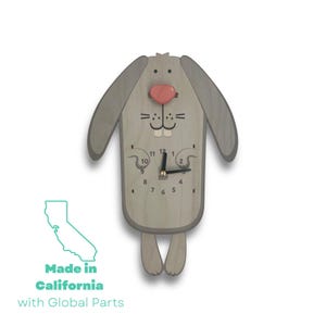 Peut inclure: Une horloge murale en bois en forme de lapin avec un nez rose et des aiguilles noires. Le cadran de l'horloge a des chiffres noirs et un fond blanc. L'horloge est fabriquée en Californie avec des pièces du monde entier.