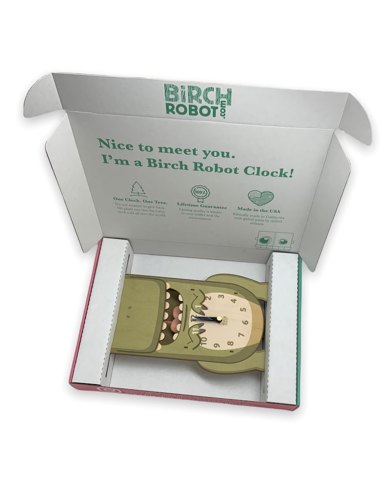 May include: A green wooden clock shaped like a monster with a toothy grin and a clock face with black hands. The clock is in an open box with the words "Birch Robot" printed on the box.