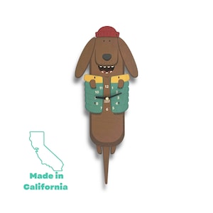 May include: A brown dachshund-shaped clock with a red hat and a green puffer vest. The clock face is visible with black hands and white numbers. The clock is made in California.