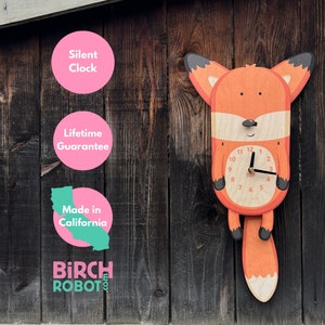 May include: A wooden fox clock with a silent movement. The clock face is white with black numbers and hands. The fox is orange with black ears and a black tail. The clock is hanging on a wooden wall. The clock is made in California and comes with a lifetime guarantee.