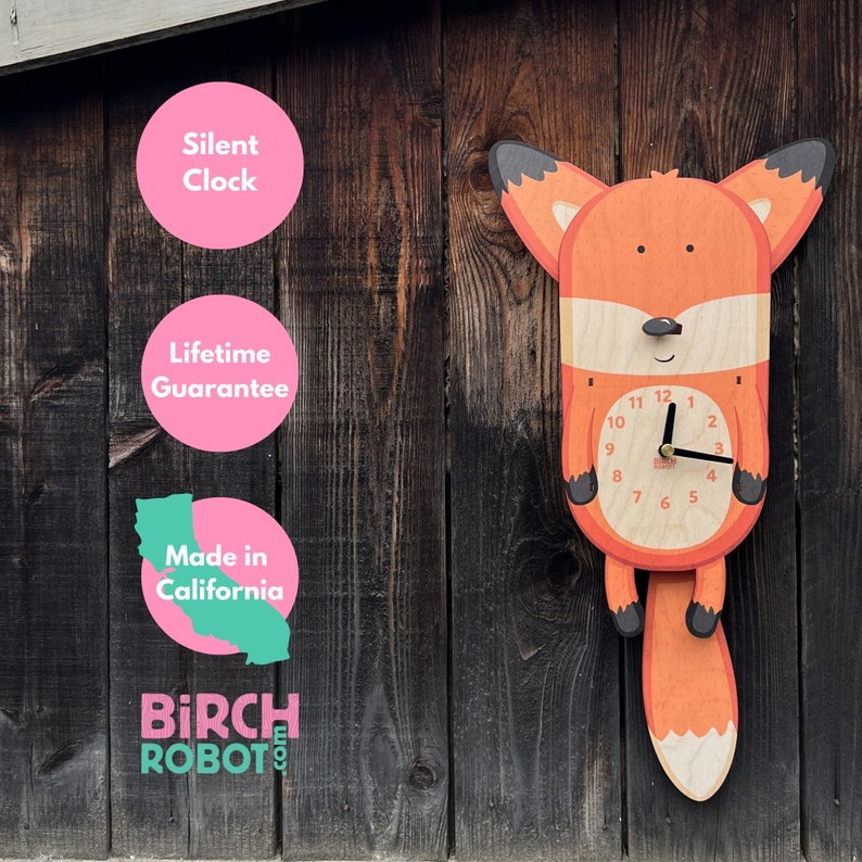 May include: A wooden fox clock with a silent movement. The clock face is white with black numbers and hands. The fox is orange with black ears and a black tail. The clock is hanging on a wooden wall. The clock is made in California and comes with a lifetime guarantee.