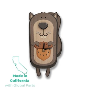 May include: A wooden squirrel-shaped clock with a brown body, a brown acorn with a clock face, and black hands. The clock face has the words "Black Forest" printed on it. The squirrel is holding the acorn in its paws. The clock is made in California with global parts.