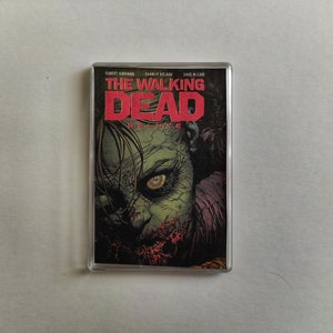 May include: A cassette tape with the cover art from "The Walking Dead" comic series. The image shows a zombie with green skin and red details. The title is in red and white lettering.