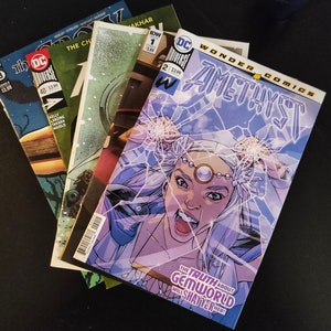 May include: A collection of comic books with colourful covers. The top comic is "Amethyst" from Wonder Comics, depicting a character breaking through a glass design. Other comics include "The Challengers" and "DC Universe".