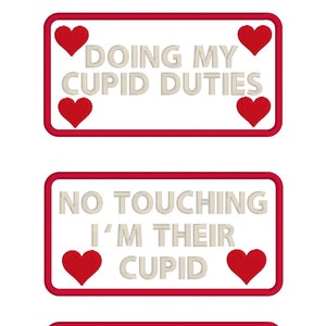 May include: Three white rectangular signs with red borders and red hearts. The signs say "Doing my Cupid duties", "No touching I'm their Cupid", and "Give us space so I can do my Cupid duties".