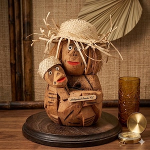 May include: A carved coconut sculpture of a mother and child wearing straw hats, with red lips and eyes. The sculpture is on a wooden base, with a tiki glass and compass nearby. The text "Hollywood Beach, FL" is visible.