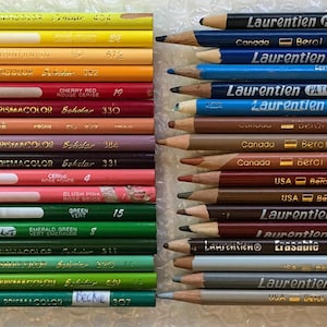 以下が含まれることがあります： 2列に並べられた42本のカラーペンシルのコレクション。ペンシルにはLaurentien、Berol Canadiana、Prismacolor Scholarなどのブランド名が記されており、それぞれの木製軸には色名と番号が印刷されています。