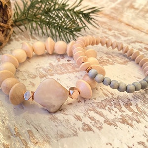 Puede incluir: Dos pulseras de cuentas de madera, una con cuentas de color marrón claro y un dije cuadrado de color marrón claro, y la otra con cuentas grises.