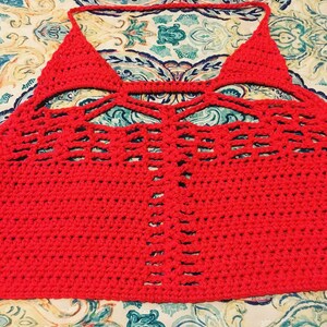 May include: A red crocheted halter top with a geometric pattern and cutouts. The top is made with a fine yarn and has a delicate, feminine look.