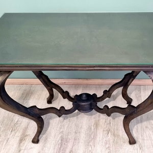 Peut inclure: Une table en bois foncé avec un plateau en verre et des pieds ornés. La table a un design unique avec un support central qui ressemble à une roue.