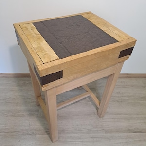 Peut inclure: Une table de bloc de boucher en bois clair avec un centre marron foncé et des pieds marron clair. La table a un dessus carré et est soutenue par quatre pieds inclinés. Le dessus est fait de plusieurs planches de bois.