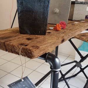 Peut inclure: Une table de bar en bois rustique avec des pieds en métal noir. La table a une finition en bois naturel et est faite de bois récupéré. La table mesure 75 cm de haut et 120 cm de long. La table est parfaite pour un petit espace ou un bar.