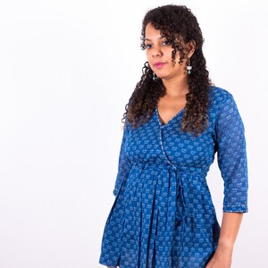 May include: A woman wearing a blue printed wrap top with a white floral pattern. The top has a tie at the waist and three-quarter sleeves. She is wearing white pants.