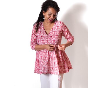 May include: A woman wearing a pink and white floral print top with a tie at the waist and white pants.