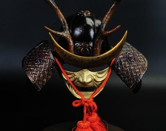 May include: A samurai helmet with a gold crescent moon and deer antlers, decorated with intricate details. The helmet is on a stand with a red tassel.